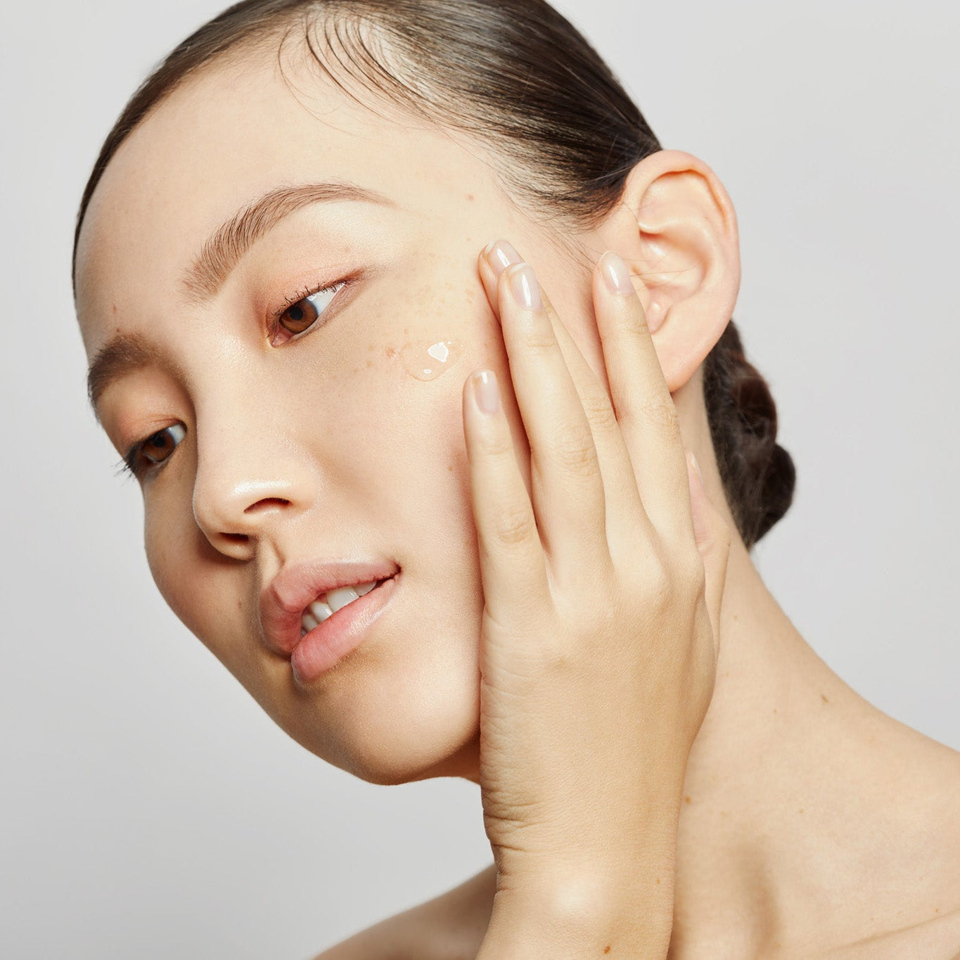 Woman applying cream to her face against a plain background