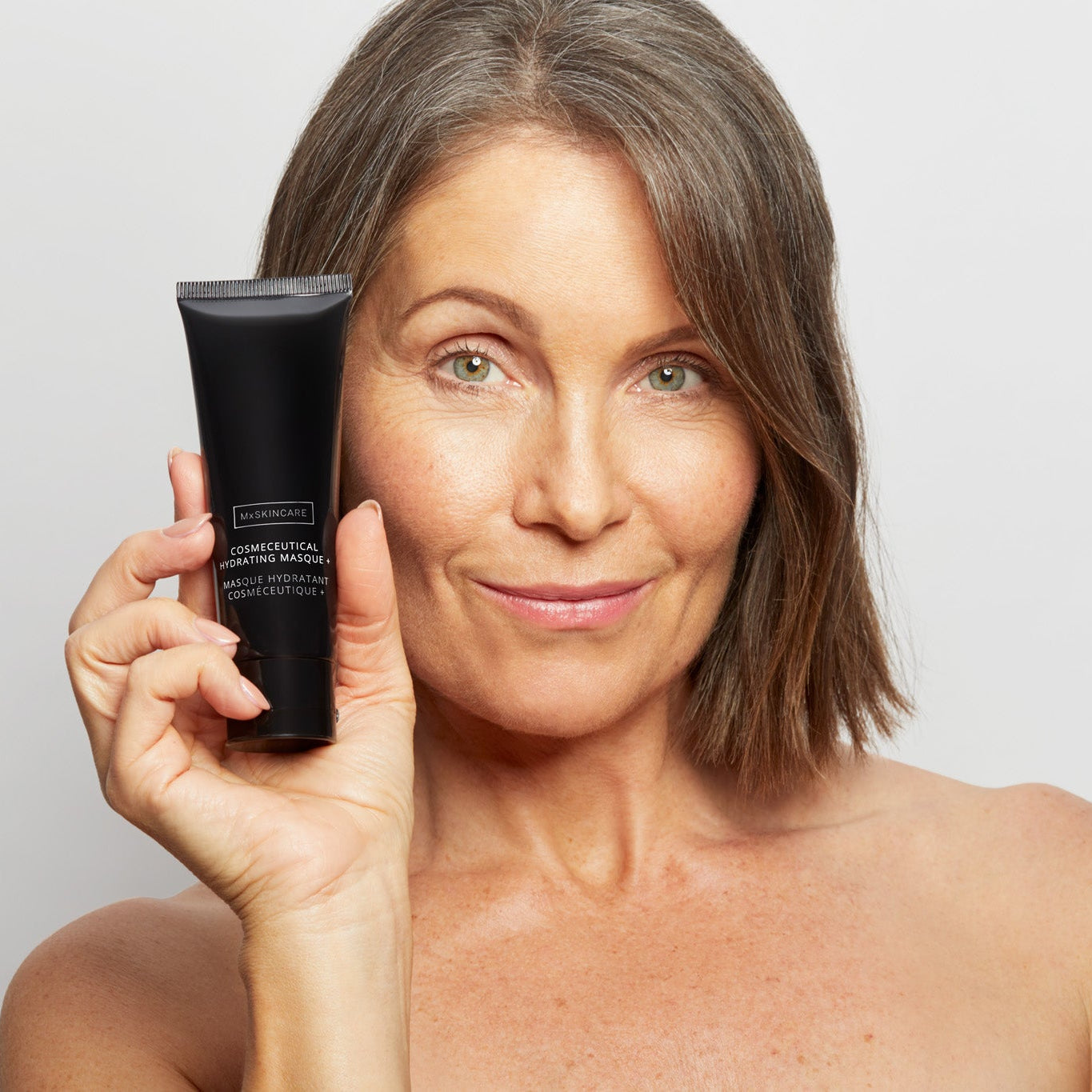 Woman holding a black mx skincare tube against a plain background