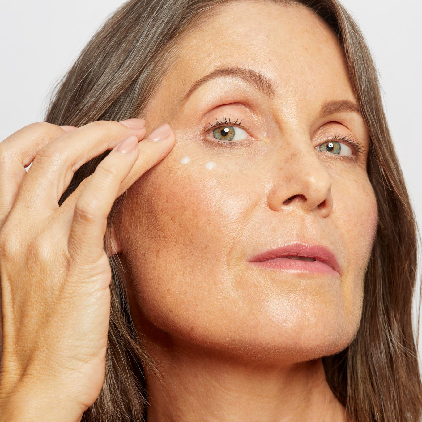 Woman applying a skincare product to her face with a neutral background