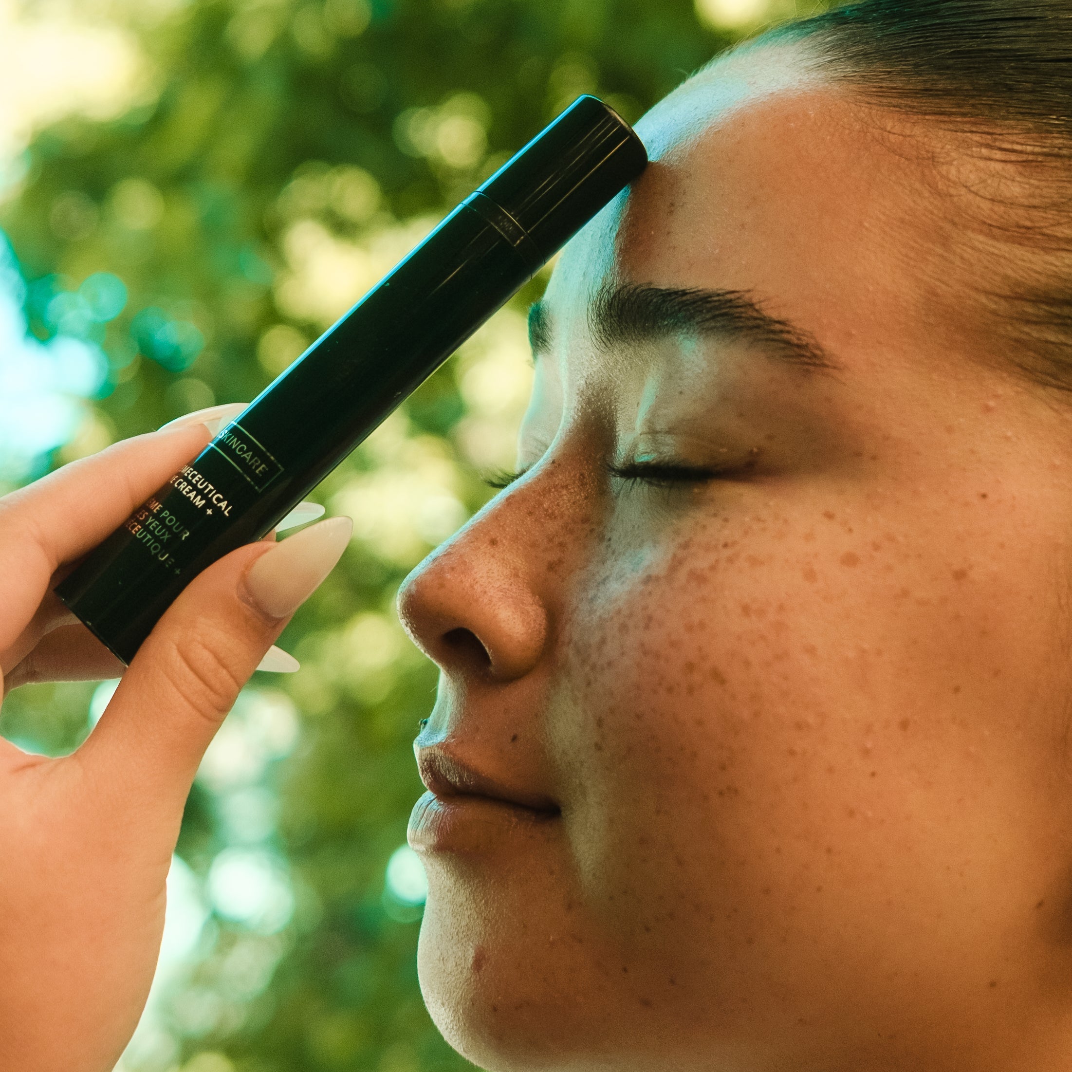 Person holding black mx skincare bottle with a blurred green outdoor background