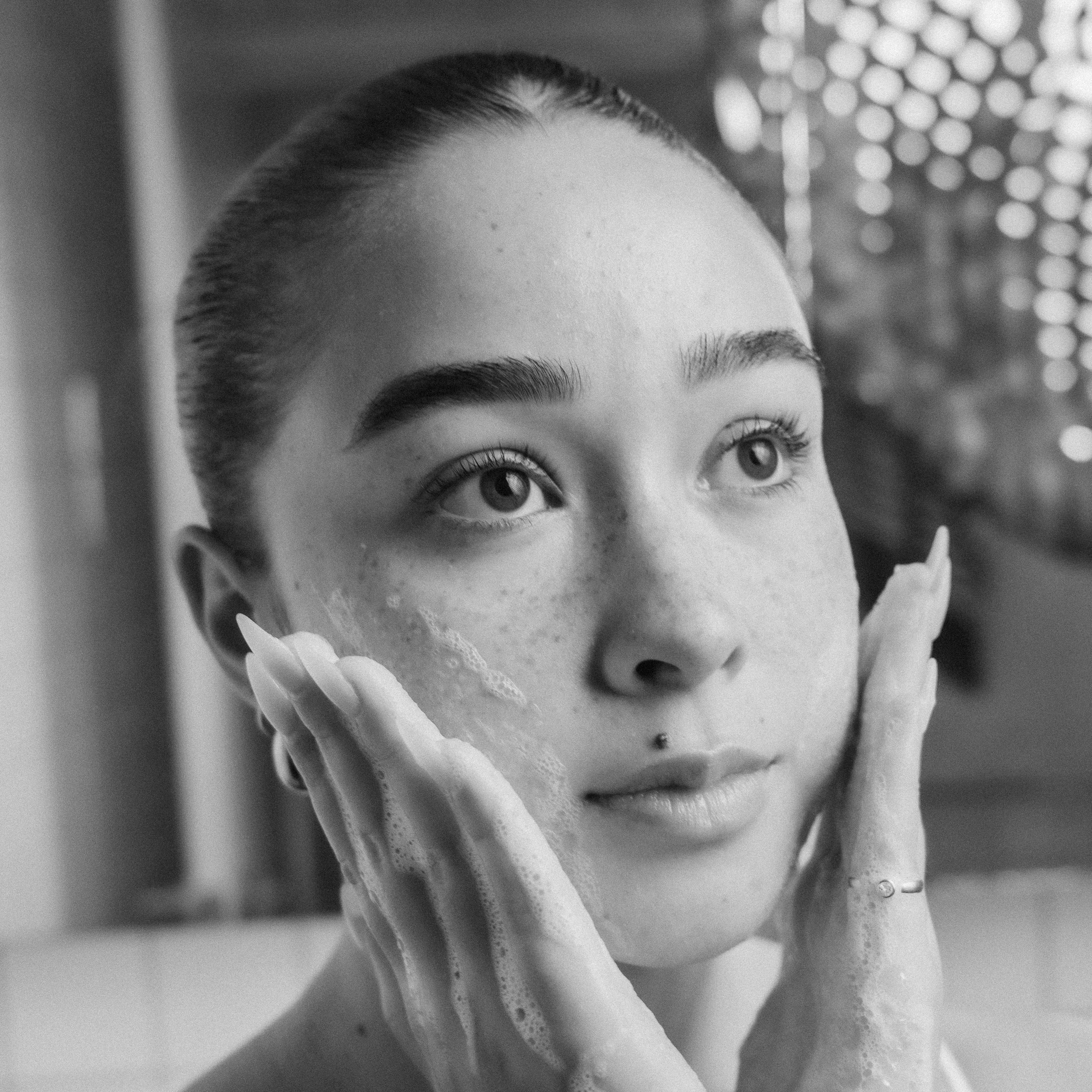 Black and white photo of a person applying skincare product to their face.