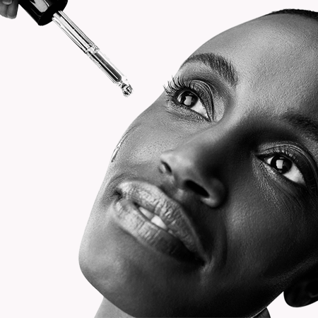 Black and white close-up of a woman's face with a dropper above her eye.