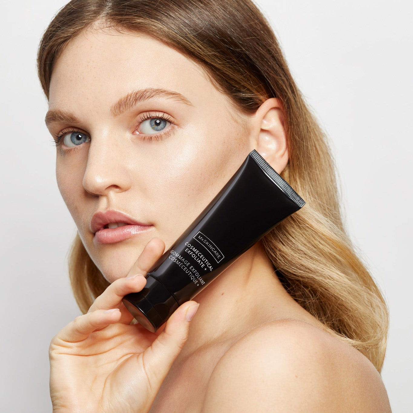 Woman holding a black mx skincare tube against a light background