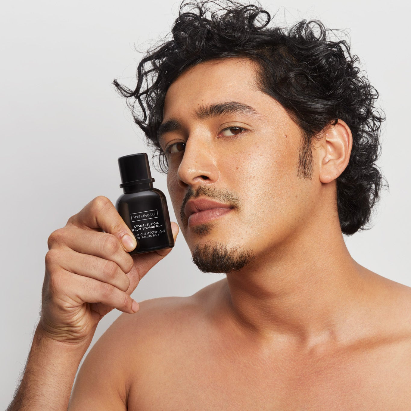 Man holding a black mx skincare bottle against a plain background