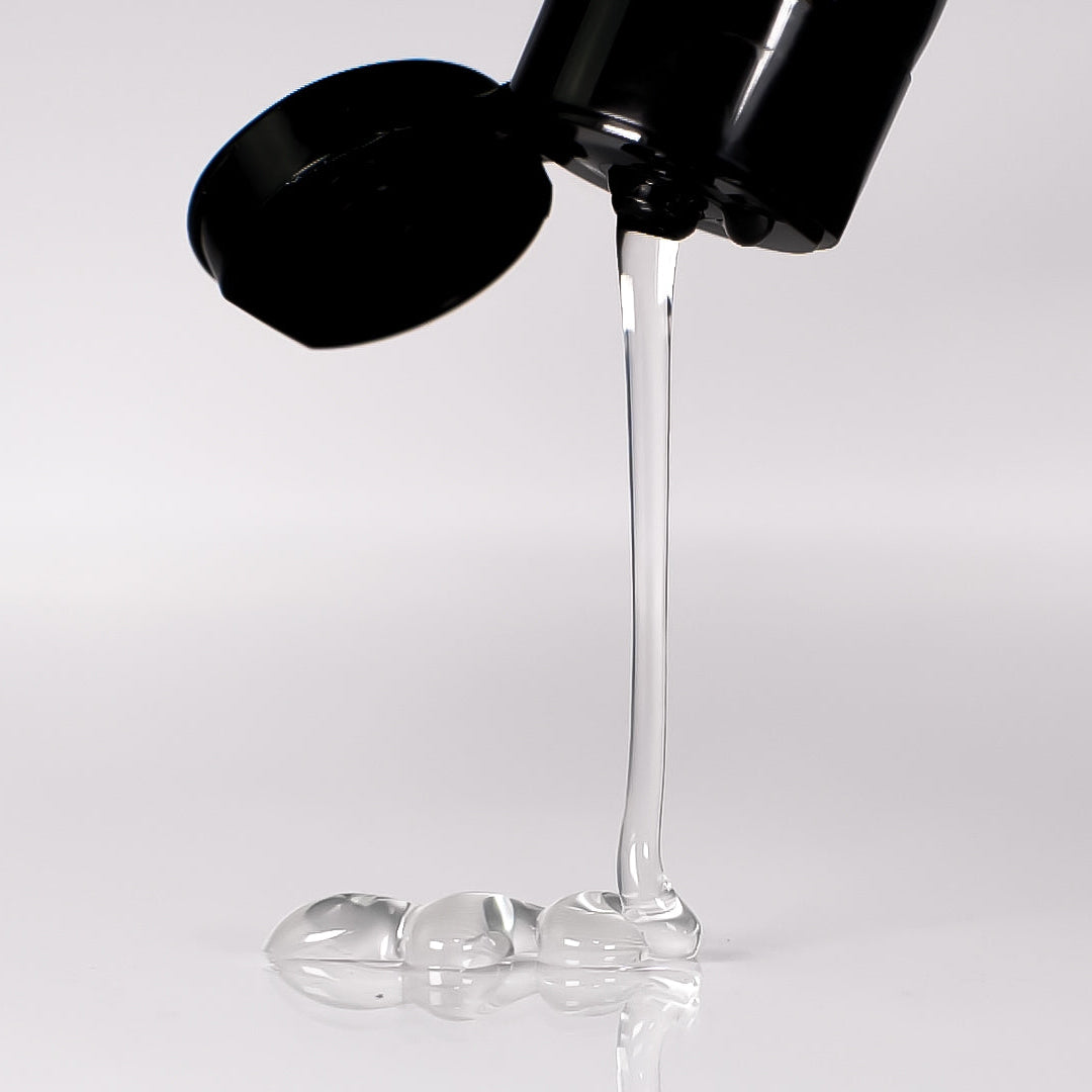 Black bottle pouring clear liquid onto a white surface